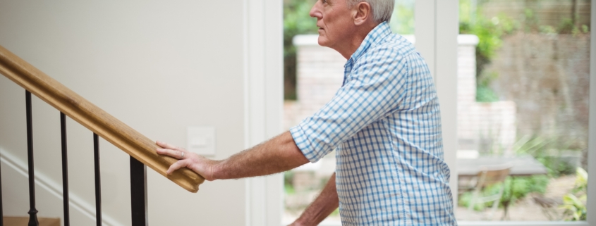 Elderly man standing at the bottom of indoor stairs
